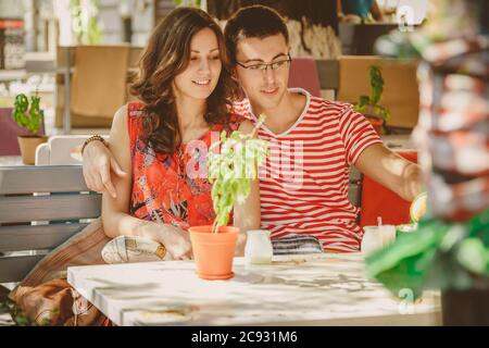 Junge schöne glücklich liebende Paar sitzt auf der Straße Open-Air-Café, umarmt. Beginn der Liebesgeschichte. Beziehung Liebe, Lifestyle-Konzept. Ein paar Stockfoto