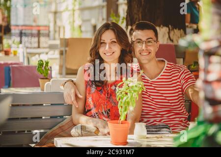 Junge schöne glücklich liebende Paar sitzt auf der Straße Open-Air-Café, umarmt. Beginn der Liebesgeschichte. Beziehung Liebe, Lifestyle-Konzept. Ein paar Stockfoto