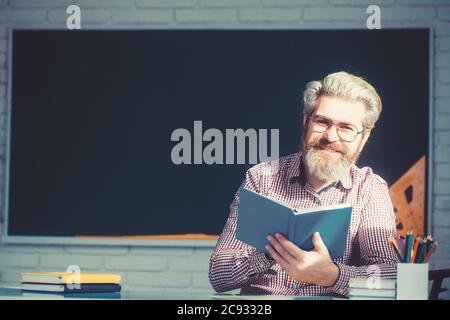 Fröhliche freundliche junge Lehrer oder Post-Graduate männlichen Schüler stehend Buch vor einem leeren Kreidetafel. Stockfoto