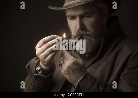 Bärtiger Mann, der Hut trägt und eine Pfeife raucht, sieht sehr ernst aus. Stockfoto