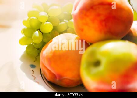 Stillleben von Trauben von zwei Pfirsichen und einem Apfel Nahaufnahme in weichem Fokus. Stockfoto