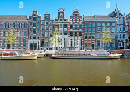 Mittelalterliche Häuser und Kreuzfahrtschiffe entlang des Kanals in Amsterdam, Niederlande Stockfoto