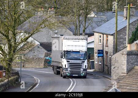 Ein in Europa registrierter Scania-LKW, der einen Curtainsider-Anhänger zieht und an einem Wintertag durch das Dorf Peak Forest in Derbyshire fährt. Stockfoto