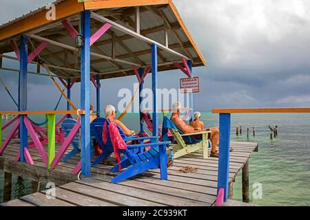 Westliche ältere Touristen in Strandliegen mit Blick auf das Karibische Meer von einem hölzernen Steg auf Caye Caulker / Cayo Caulker, Insel vor der Küste von Belize Stockfoto