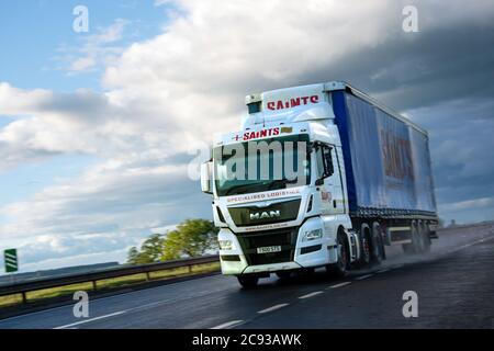 MAN TGX LKW zieht Curtainsider Anhänger auf einer zweispurigen Fahrbahn In Schottland im Regen mit Wolken dahinter Stockfoto