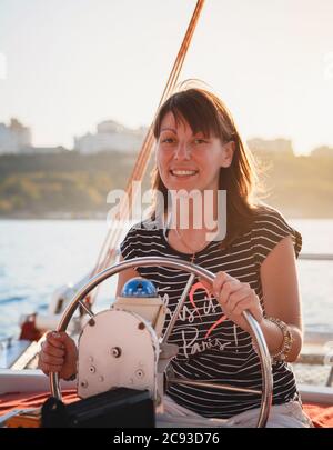 Junge hübsche lächelnde Frau im gestreiften Hemd fahren Luxus-Yacht im Meer, Sonnenuntergang Stockfoto