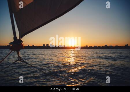 Sonnenuntergang über der Stadt vom Segelboot. Segelboot Winde, Segel und nautische Seil Yacht Detail. Yachting, marine Hintergrund Stockfoto