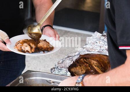 Ein Mann, der Sauce für ein gegrilltes Ferkel / Spangen serviert, mit der Haut noch darauf. Stockfoto