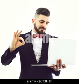 Geschäftsmann oder TV-Ansager zeigt OK Zeichen und hält weißen Laptop. Lächelndes Gesicht, isoliert auf weißem Hintergrund. Konzept des kontrollierten Geschäfts und der Technologie Stockfoto
