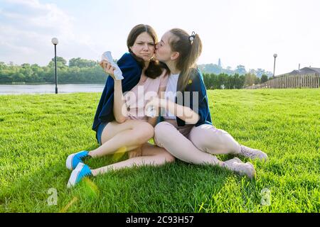 Weinende Teenager Mädchen und tröstende Freundin, Jugendliche auf dem Gras im Park sitzen Stockfoto