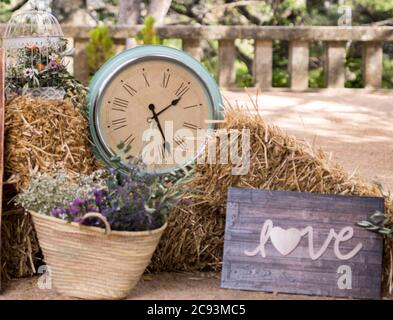 Holzbrett mit dem Wort "Liebe", eine Vintage-Uhr und ein Strohkorb mit Blumen Stockfoto