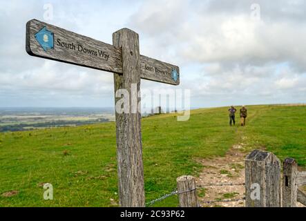 South Downs National Park, Sussex, Großbritannien in der Nähe von Firle Beacon. Ein Wegweiser zeigt die Route der South Downs Way mit zwei unkenntlichen Wanderern. Stockfoto