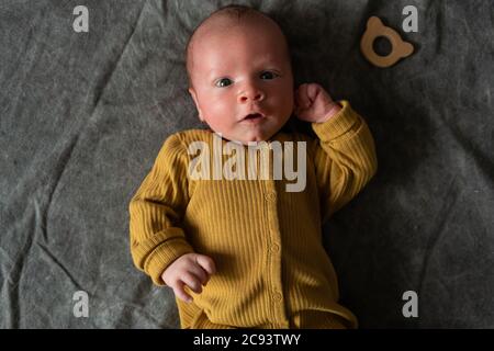 Ein Monat Neugeborenes mit offenen Augen liegt auf dem Rücken auf grauem Hintergrund. Nahaufnahme Porträt von niedlichen kleinen Jungen. Stockfoto