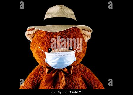 Teddybär trägt einen Panamahut und Gesichtsmaske isoliert auf schwarzem Hintergrund Stockfoto