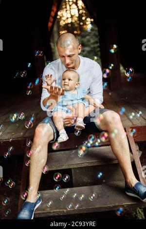 Fürsorglicher Vater halten kleine Tochter, niedlichen Kleinkind versuchen, die Blasen zu fangen Stockfoto