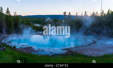 Bäume spiegeln sich im Abendlicht in einem Thermalbecken im Norris Geyser Basin, Yellowstone National Park Stockfoto