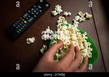 Schwarze Fernbedienung mit etwas Popcorn auf einem braunen Tisch Stockfoto