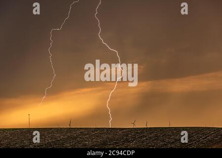 Ein Gewitter bei Sonnenuntergang passiert die Great Plains, während strömender Regen und knackende Blitze den Horizont markieren. Stockfoto