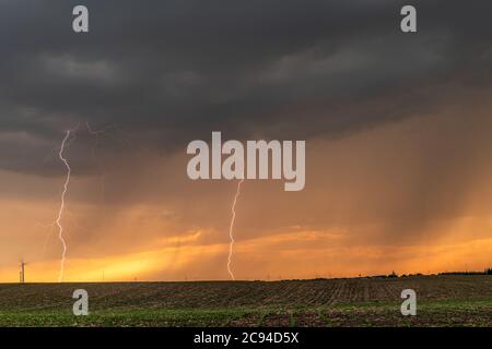 Ein Gewitter bei Sonnenuntergang passiert die Great Plains, während strömender Regen und knackende Blitze den Horizont markieren. Stockfoto