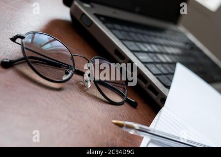 Laptop und schwarze Brille mit einem Notebook auf einem Holz Schreibtisch Stockfoto