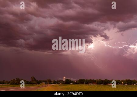 Ein Gewitter bei Sonnenuntergang passiert die Great Plains, während strömender Regen und knackende Blitze den Horizont markieren. Stockfoto