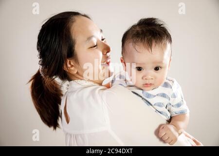Asiatische Mutter hält Baby Sohn Porträt, glücklich vietnamesischen Eltern mit Kleinkind Kind Blick über die Schulter, weißer Hintergrund Stockfoto