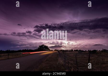 Ein Gewitter über den Great Plains bietet eine dramatische Lichtshow in der Nacht als ein Auto Rücklichter Streifen durch das Bild. Stockfoto