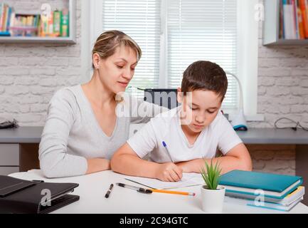 Mutter hilft Sohn, Unterricht zu machen. Der Tutor ist mit dem Kind beschäftigt Stockfoto