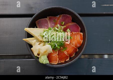 Draufsicht, Japanische Maguro, Thunfisch und Lachs Reis Schale oben mit japanischem gerolltem Omelett und Zwiebel, auf Holztisch. Stockfoto