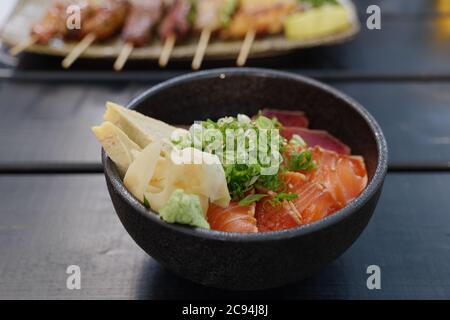 Draufsicht, Japanische Maguro, Thunfisch und Lachs Reis Schale oben mit japanischem gerolltem Omelett und Zwiebel, auf Holztisch. Stockfoto