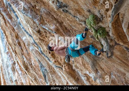 Blick auf den Bergsteiger in leuchtend blauen Hosen, der die anspruchsvolle vertikale Route an einer felsigen Wand klettert Stockfoto