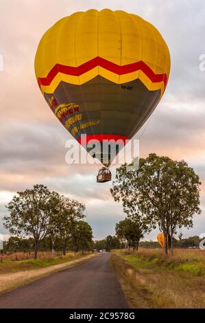 Eine bunte Luftballons mit Touristen, beginnt es Morgendämmerung Abenteuer langsam steigt über Bäumen und einer Landstraße in Mareeba, Queensland, Australien. Stockfoto