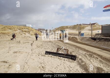 Eine Planierraupe schiebt den Sand am Eingang zum Strand von Bergen aan Zee. Viel Wind. Niederlande, März Stockfoto