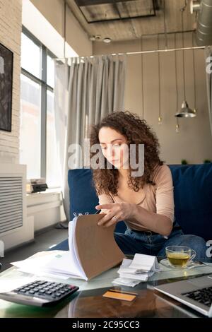 Fokussierte, lockige junge Frau, die in soziale Medien auf dem Laptop tippt, während sie im Café online interagiert Stockfoto