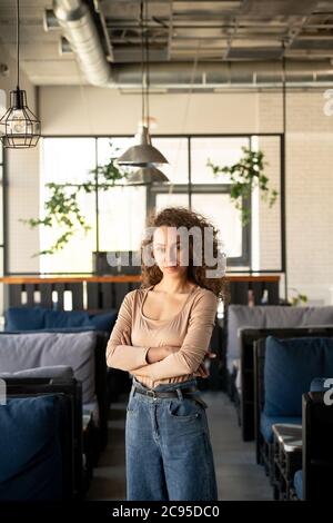 Porträt des Inhalts lockig-haarige Unternehmer stehen mit gekreuzten Armen in eigenen gemütlichen Café Stockfoto