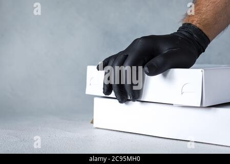 Lieferung nach Hause, Online-Bestellung. Gummihandschuhe mit einer Box, mit einem Paket in den Händen. Lebensmittel- und Lebensmittelzustellung während der Quarantäne Stockfoto
