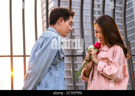 Junge glückliche Paare lieben und romantisch auf den ersten Tag Beziehung: asiatische Teenager-Frau überrascht und lächelt an Freund gibt rote Rosen-Blumen auf Dinne Stockfoto