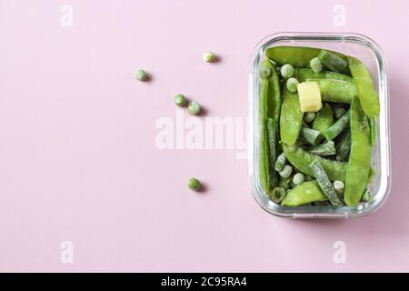 Gefrorenes Gemüse wie grüne Hülsen und Erbsen in den transparenten Schalen auf dem rosa Hintergrund mit Copyspace. Draufsicht. Stockfoto