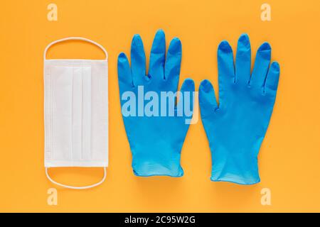 Stock Foto von einer Gesichtsmaske und ein Paar blaue Latex-Handschuhe auf einem gelben Hintergrund. Coronavirus-Prävention Stockfoto