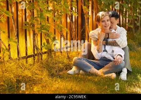Zwei glückliche Freundinnen sitzen auf dem Gras im Park und umarmen sich Stockfoto