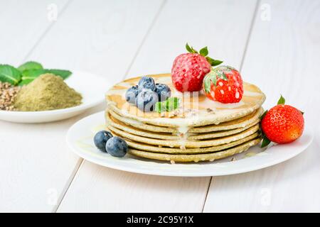 Auf einem Teller befindet sich ein Stapel Pfannkuchen aus Mehl und Hanfsamen. Heidelbeere und Erdbeere Belag. Mit Kondensmilch gegossen. Vegane Küche Stockfoto