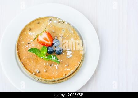 Auf einem Teller ist ein Stapel Hanfmehl Pfannkuchen. Dekoriert mit Heidelbeeren, Erdbeeren, Hanfsamen und Minze. Mit Puderzucker bestäubt. Flach liegend Stockfoto