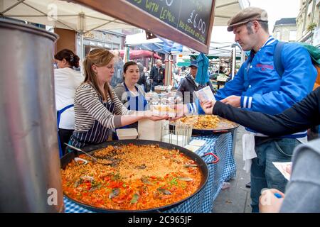 London, Großbritannien - Straßenszene auf dem Markt in der Portobello Road. Eine junge Marktfrau verkauft Paella an ihrem Marktstand. Der Markt in Notting Hi Stockfoto