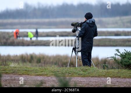 Mann (Vogelbeobachter) steht mit dem Teleskop auf Stativ und Freiwillige arbeiten in Feuchtgebieten Lebensraum - St. Aidan's RSPB Naturpark, Leeds, Yorkshire, England, UK Stockfoto