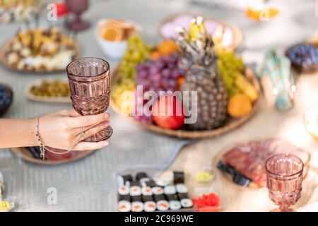 Eine Hand von Frau hält ein Glas auf dem Gourmet-Picknick im Hintergrund Stockfoto