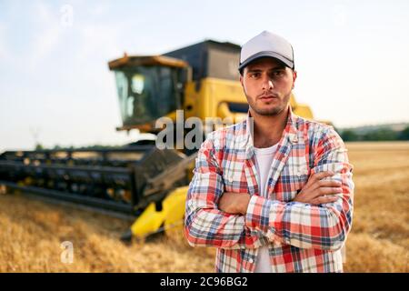 Portrait des stolzen Harvester-Maschinentreibers mit gekreuzten Händen auf der Brust. Bauer steht an seinem Mähdrescher. Agronom schaut auf die Kamera. Rancher bei Stockfoto