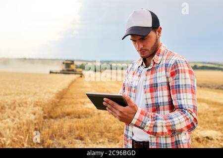 Präzisionslandwirtschaft. Landwirt hält Tablet für Mähdrescher Führung und Steuerung mit modernen Automatisierungssystem. Agronom mit Online-Daten Stockfoto