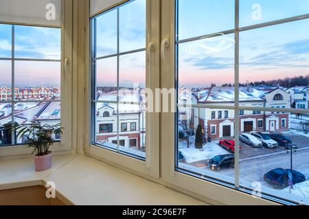 Blick aus dem Fenster einer Stadtwohnung auf einen landschaftlich gestalteten Innenhof im Winter bei Sonnenuntergang. Moderne städtische Immobilien und Eigentumswohnungen Architektur. Stockfoto