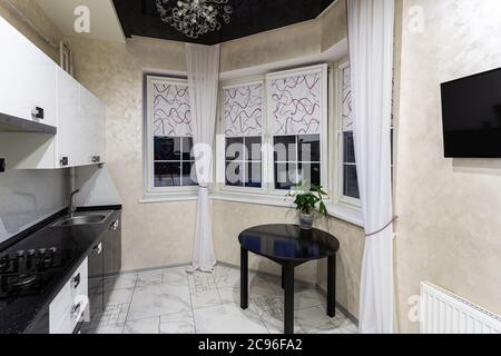 Gemütliche moderne Küche in kleinen Wohnungen. Weiße Möbel mit schwarzer Platte und einem Esstisch aus Holz. Innenarchitektur. Stockfoto