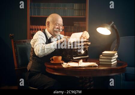 Lächelnder älterer Schriftsteller arbeitet auf Retro-Schreibmaschine Stockfoto